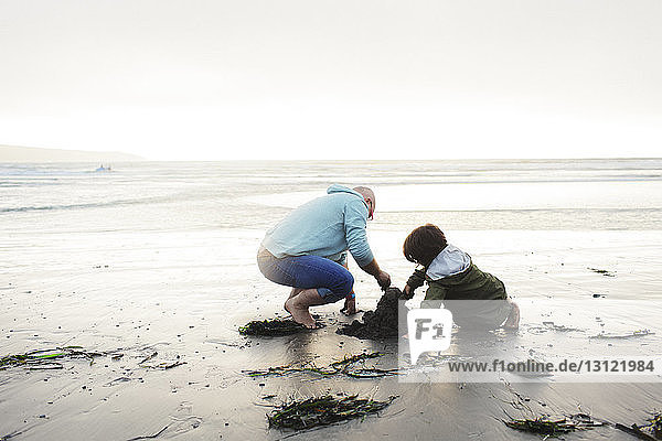 Vater und Sohn spielen mit Sand am Strand vor klarem Himmel
