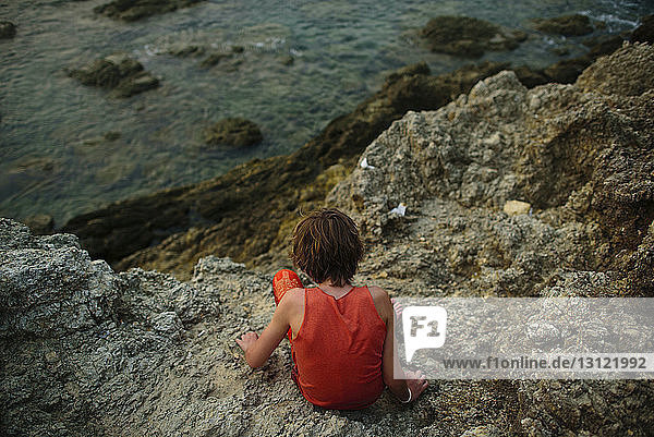 Hochwinkelaufnahme eines Jungen,  der auf Felsen im Meer sitzt