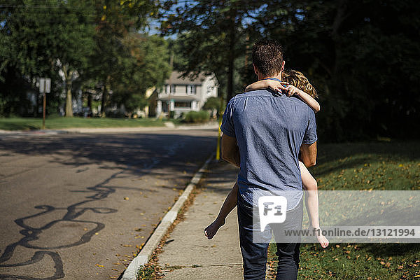 Rear view of father carrying daughter while walking on footpath