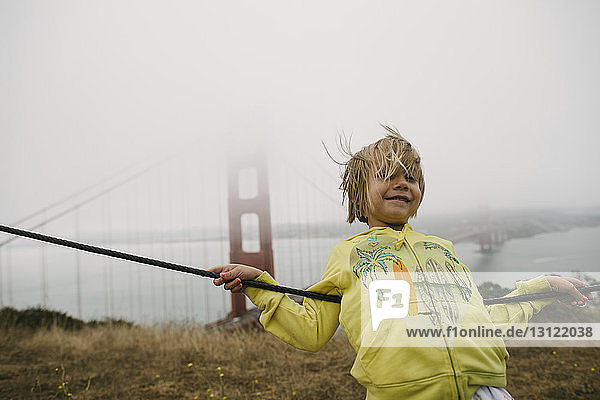 Mädchen lehnt bei nebligem Wetter am Kabel gegen die Golden Gate Bridge