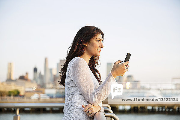 Seitenansicht einer Frau  die ein Smartphone hält  während sie bei Sonnenuntergang am Beobachtungspunkt steht