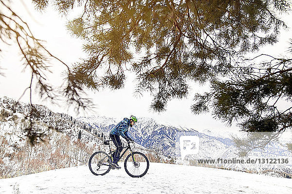 Side view of man riding bicycle on snow covered mountain against sky