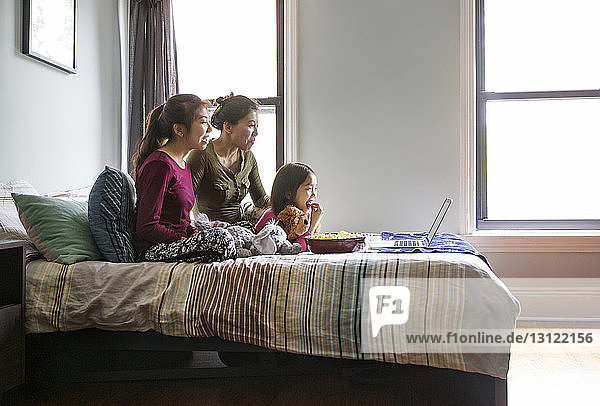 Familie schaut zu Hause auf dem Laptop im Bett einen Film an