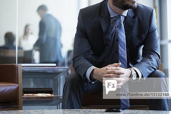 Mittelteil eines Geschäftsmannes  der mit gefalteten Händen auf einem Sessel im Büro sitzt