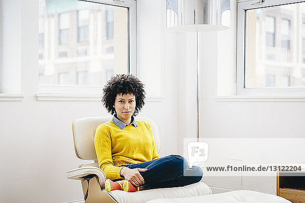 Porträt einer selbstbewussten Geschäftsfrau  die auf einem Stuhl im Büro sitzt