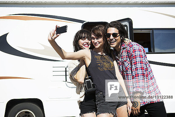 Friends taking selfie while standing by camper van