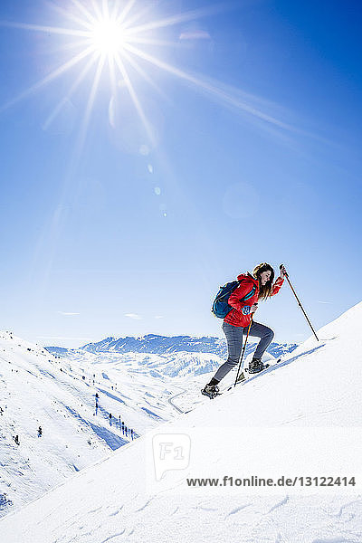 Weibliche Wanderin klettert bei Sonnenschein auf schneebedeckten Berg gegen den Himmel
