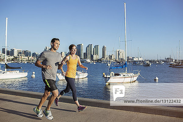 Happy male and female athletes jogging on pier by harbor