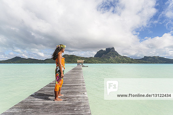 Frau in traditioneller Kleidung steht auf Steg über der Lagune vor bewölktem Himmel