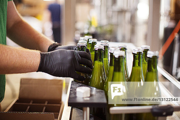 Beschnittenes Bild von Händen  die Bierflaschen auf einem Förderband in einer Brauerei arrangieren