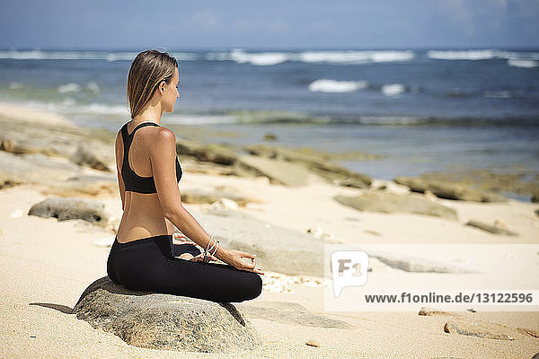 Seitenansicht einer Frau  die im Sommer in Lotusstellung am Strand meditiert