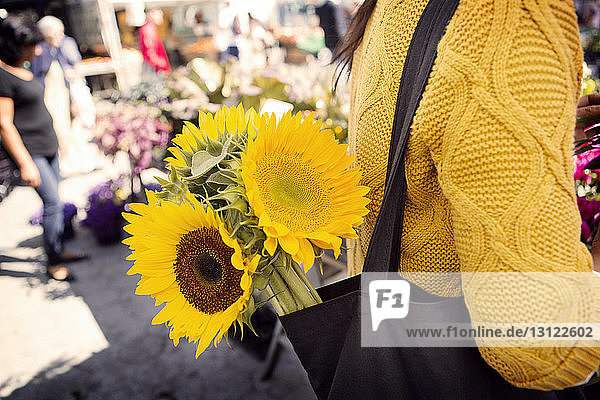 Midsection of woman carrying sunflowers in purse at market