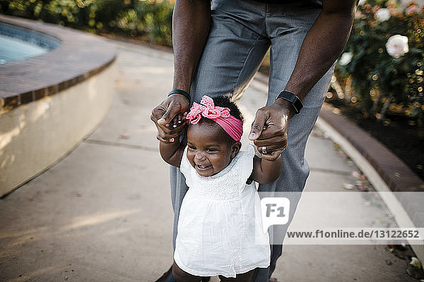 Mitschnitt eines Vaters  der seiner Tochter beim Gehen auf einem Fußweg im Park hilft