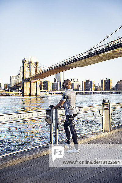 Männlicher Athlet in voller Länge auf der Promenade stehend mit der Brooklyn Bridge im Hintergrund