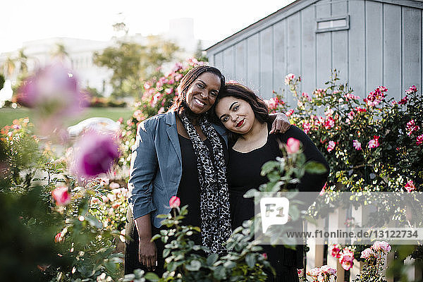 Porträt von glücklichen Schwestern  die inmitten von Pflanzen im Park stehen