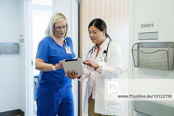 Ärztinnen diskutieren über Tablet-Computer  während sie im Krankenhaus an der Wand stehen