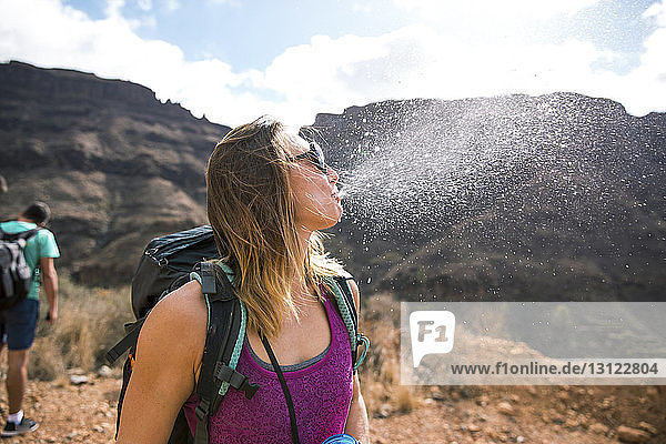 Female backpacker spitting water against mountains at desert