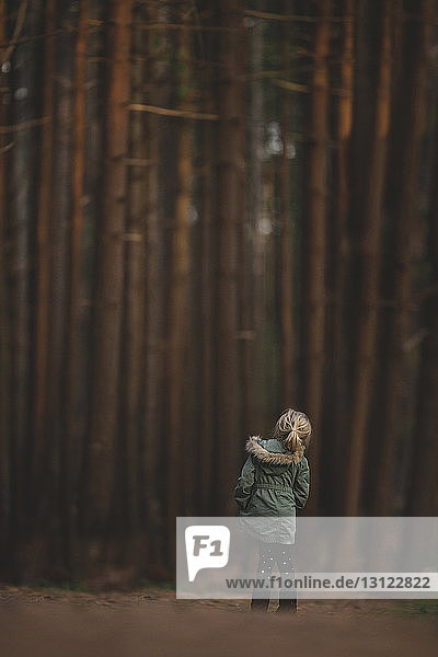 Rear view of girl standing against trees at forest
