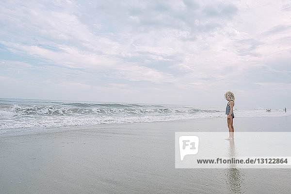 Full length of girl standing at Cape May Beach against cloudy sky
