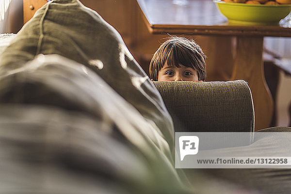 Porträt eines süßen Jungen  der sich zu Hause hinter einem Sofa versteckt