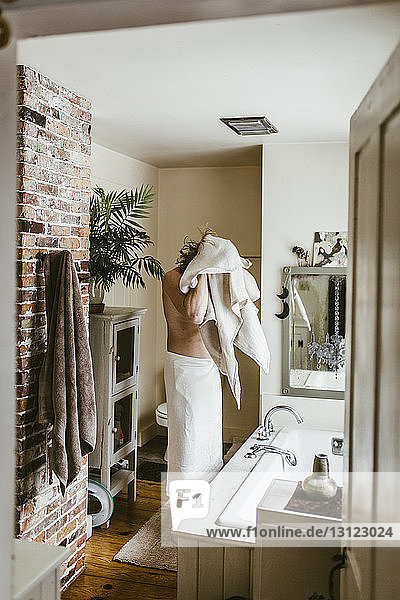 Mann ohne Hemd  der die Haare mit einem Handtuch trocknet  während er im Badezimmer steht  durch die Tür gesehen