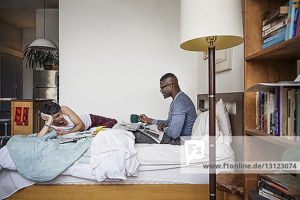 Gay men talking while reading newspaper in bedroom