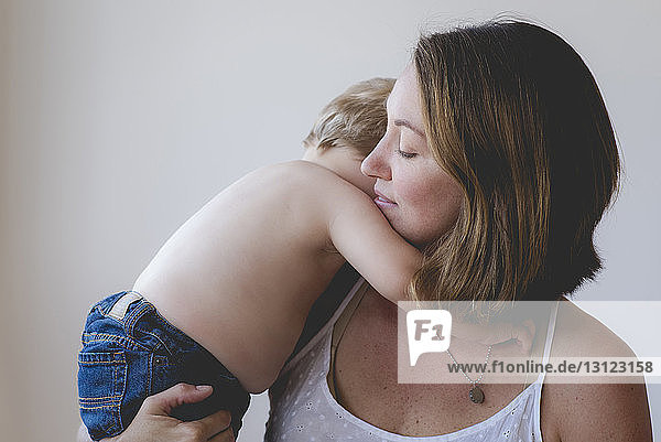 Mother carrying shirtless son against white background