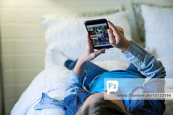 Girl using smart phone while lying on bed at home