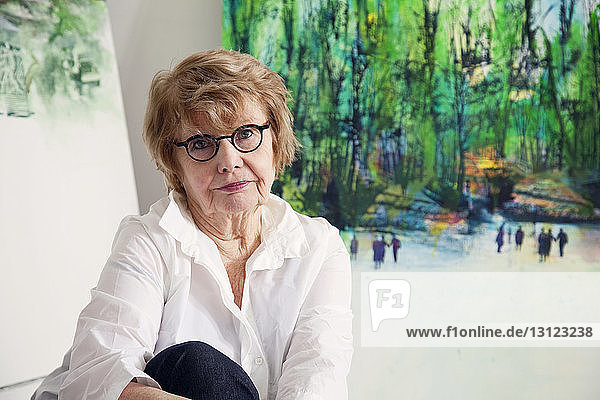 Porträt einer älteren Frau  die zu Hause gegen Gemälde sitzt