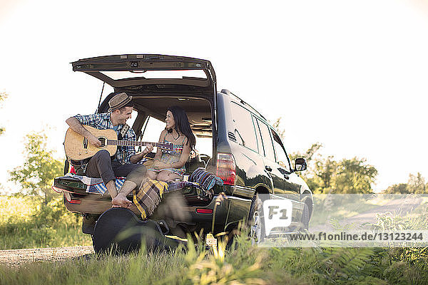 Man playing guitar for girlfriend while sitting in car