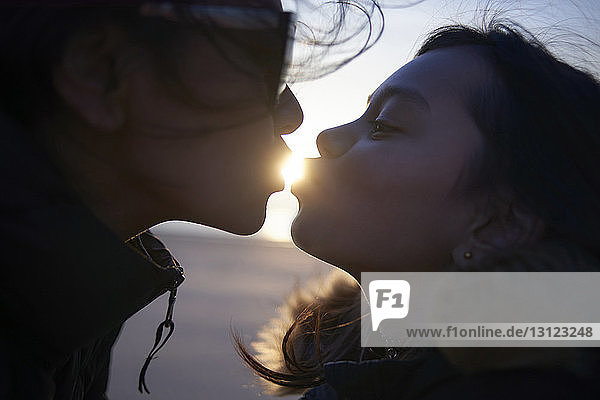 Optische Täuschung von Schwestern  die bei Sonnenuntergang am Strand die Sonne küssen