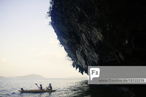 Mother with children kayaking in sea by rock