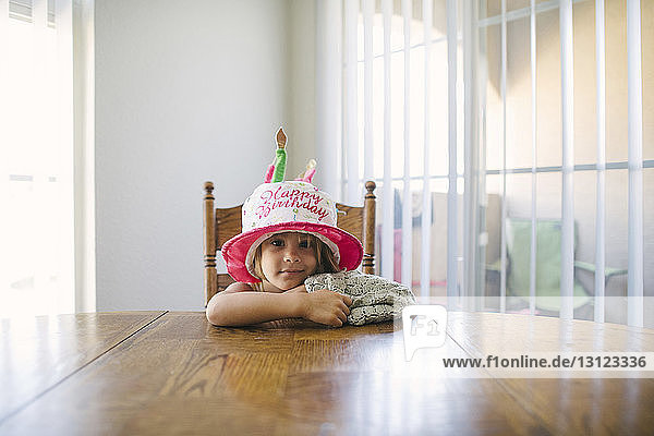 Porträt eines Mädchens mit Hut mit Geburtstagsglückstext bei Tisch sitzend