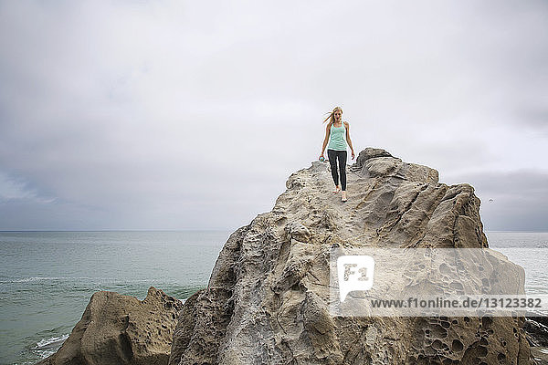 Frau in voller Länge beim Abstieg von Felsen am Meer gegen klaren Himmel