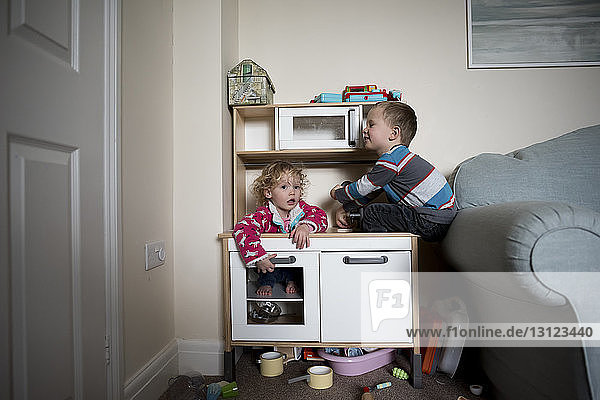 Siblings playing on cabinet by sofa at home