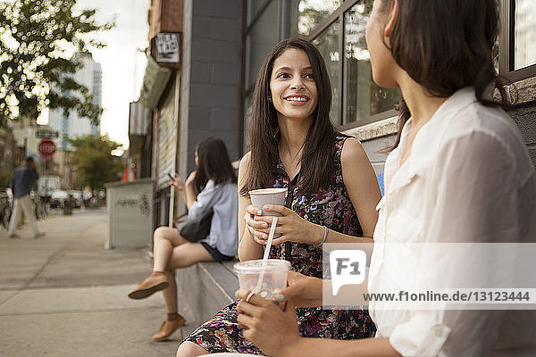 Lächelnde Freunde trinken Kaffee  während sie vor einem Café sitzen