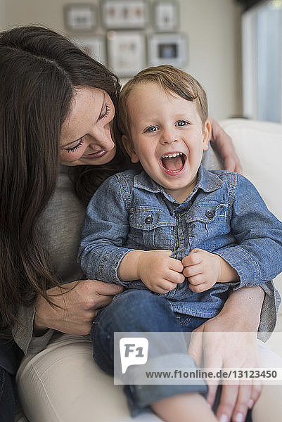 Porträt eines Jungen  der schreit  während er bei seiner Mutter zu Hause sitzt