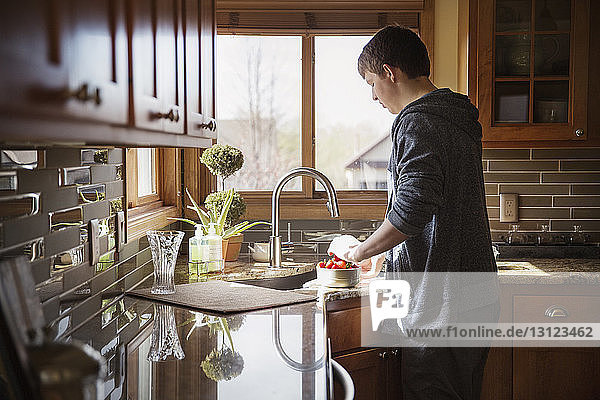 Rückansicht eines jungen Mannes  der in der Küche Erdbeeren wäscht