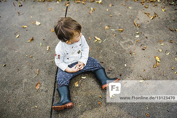Hochwinkelaufnahme eines kleinen Jungen  der im Herbst auf einem Fußweg sitzt