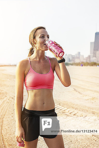 Weibliche Sportlerin trinkt Wasser  während sie am Strand steht