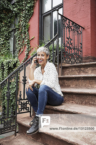 Porträt einer glücklichen Frau  die auf einer Treppe sitzend mit ihrem Handy telefoniert