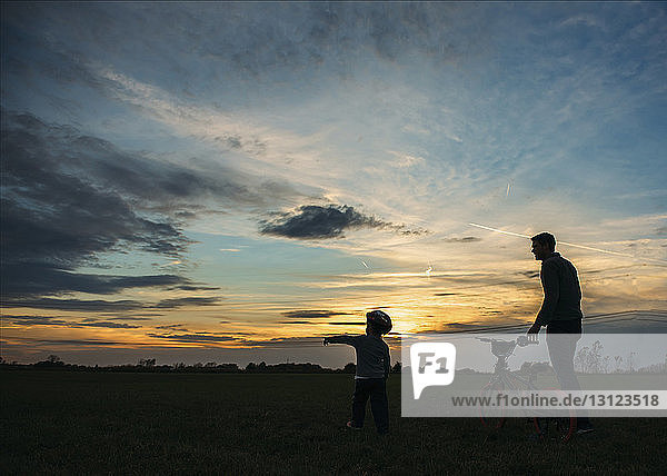 Silhouette father and son walking with bicycle on field during sunset