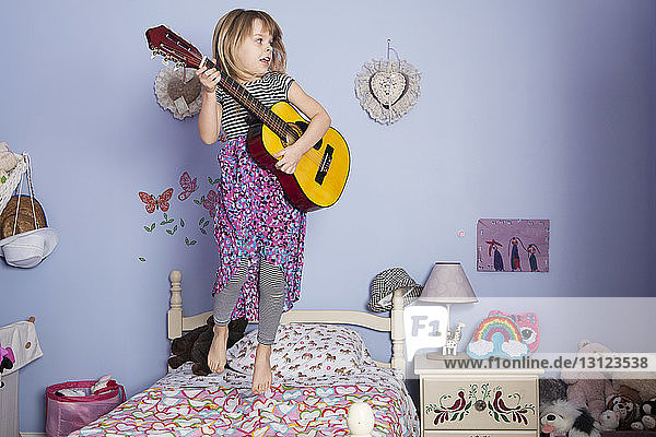 Mädchen hält Gitarre und springt auf dem Bett