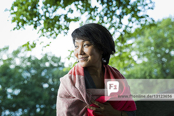 Glückliche Frau in eine Decke gewickelt an Bäumen