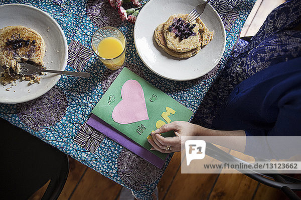 Overhead view of woman eating pancakes by greeting cards on table on birthday