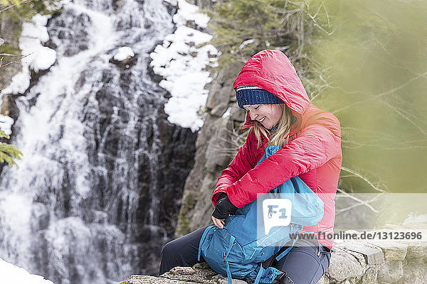 Smiling woman with backpack sitting against waterfall at White Mountains during winter