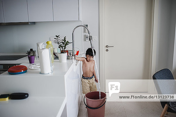 Junge ohne Hemd füllt zu Hause Wasser in Eimer