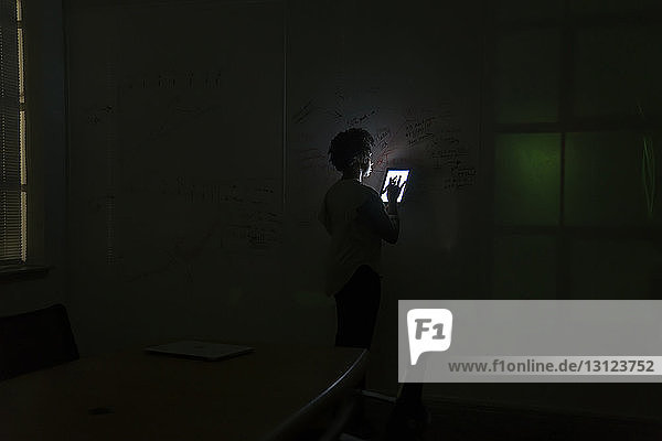 Geschäftsfrau benutzt Tablet-Computer  während sie im dunklen Büro an der Tafel steht