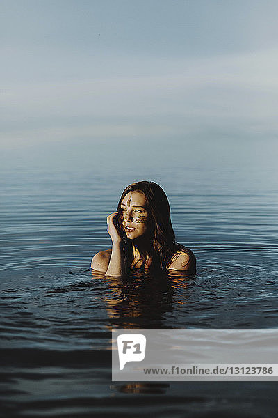 Junge Frau mit Schlamm im Gesicht schaut weg  während sie im See gegen den Himmel schwimmt