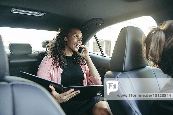 Geschäftsfrau spricht mit einem Smartphone  während sie eine Akte im Auto hält